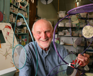 A man posing with various pieces of art he created