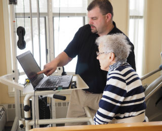 Man showing information to an elderly woman on a laptop