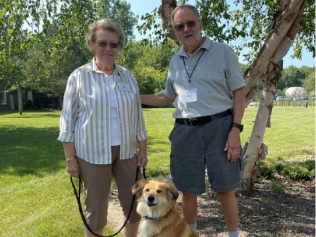 man and woman standing under tree with dog 