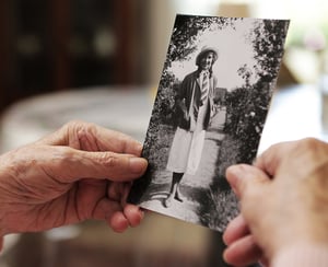  Older woman holding up an old photograph reflecting on her life while downsizing