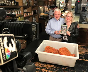  Author standing with book in a Cleveland kitchen in front of a tv camera